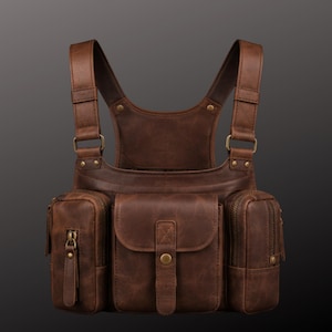 Può includere: Un pettorale in pelle marrone con due spallacci verticali, una tasca centrale con chiusura a bottone automatico e due scomparti laterali con chiusure a zip. Il design presenta finiture in metallo color ottone e cuciture a vista.