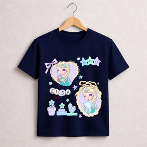 May include: A navy blue t-shirt with a cartoon illustration of Elsa from Frozen. The design includes Elsa's name, stars, and other decorative elements. The shirt is made of a soft, comfortable material.