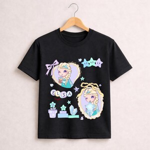 May include: Black t-shirt with a cartoon illustration of Elsa from Frozen. The design includes Elsa's image, stars, and the name "ELSA". The shirt has a crew neck and short sleeves. The graphic is in pastel colours.