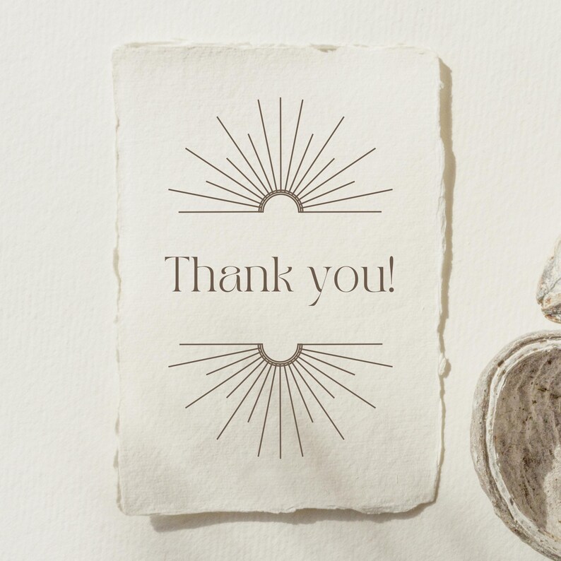 Op de afbeelding: Een cr&egrave;mekleurige kaart met een geschulpte rand met de woorden "Thank you!" in een schreefletter. Boven en onder de tekst staan symmetrische sunburst-ontwerpen in donkerbruin. De kaart heeft een minimalistisch, elegant ontwerp.