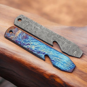 May include: Two metal bottle openers with a unique design. One is a silver color with a swirling pattern, and the other has a blue and purple iridescent finish. Both have a hole for a keychain.