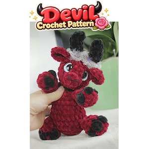 Pode incluir: Um brinquedo de pelúcia de diabo feito em crochê com fio vermelho escuro, chifres pretos, cascos pretos e olhos grandes e brilhantes. A cabeça é adornada com um tufo de fio cinza. Acima, um gráfico exibe o texto Devil Crochet Pattern.