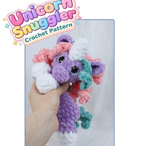 May include: A handmade crochet unicorn plushie in shades of purple, pink, teal, and white. The unicorn has a fluffy mane and tail, with the text "Unicorn Snuggler Crochet Pattern" in a colorful banner.