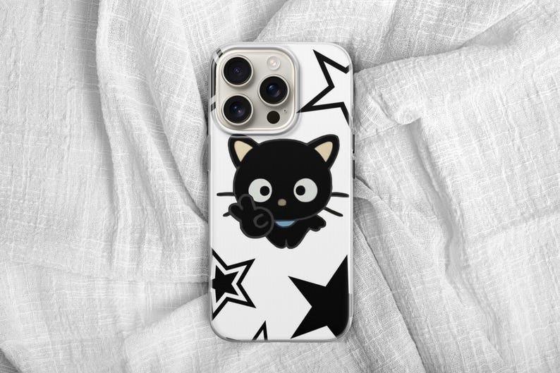 Op de afbeelding: Een witte telefoonhoes met een zwart cartoonkatontwerp dat een vredesteken geeft, en zwarte stervormen. De telefoonhoes heeft een cameramodule met drie lenzen.