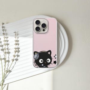 Op de afbeelding: Een roze telefoonhoesje met een zwarte kat met een koptelefoon en sterren. Het telefoonhoesje ligt op een wit bord met gedroogde bloemen links.