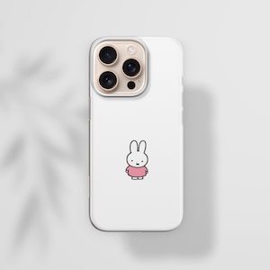 May include: White phone case featuring a cartoon bunny wearing a pink dress. The phone case has a clear border and a camera module with three lenses. The background is a light gray with a shadow of leaves.