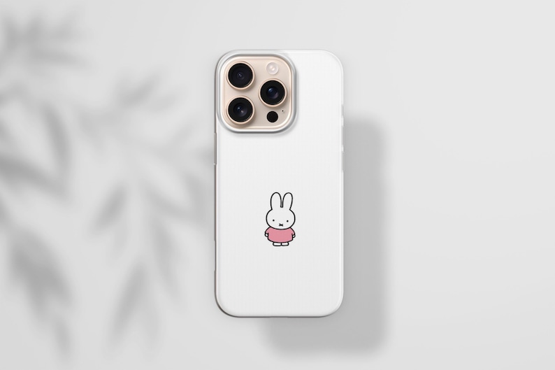May include: White phone case featuring a cartoon bunny wearing a pink dress. The phone case has a clear border and a camera module with three lenses. The background is a light gray with a shadow of leaves.