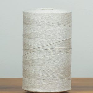 May include: A large spool of natural-coloured twine. The twine is tightly wound around a cylindrical core, creating a solid, textured appearance. The neutral colour and construction suggest its use in crafts or packaging.