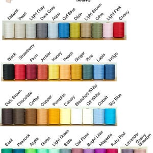 Op de afbeelding: Een collectie van 8/2 katoengaren op spoelen, gerangschikt in vier rijen, elk gelabeld met kleurnamen waaronder Naturel, Pearl, Light Gray, Dark Gray, Aqua, Old Blue, Dijon, Light Brown, Olive, Light Pink, Cherry, Black, Strawberry, Plum, Amber, Honey, Peach, Ginger, Pine, Lapis, Indigo, Dark Brown, Chocolate, Coffee, Copper, Pumpkin, Canary, Bleached White, Off White, Cobalt, Sky Blue, Basil, Peacock, Apple, Green, Light Green, Slate, Old Rose, Bright Lilac, Magenta, Ruby Red, Lavender en Cherry Blossom.