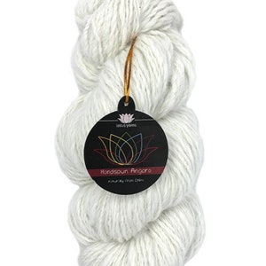 May include: A skein of white handspun angora yarn, naturally sourced from China. The yarn is packaged with a circular tag that reads "Lotus Yarns" and "Handspun Angora" with a colourful lotus flower logo.