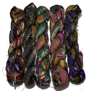May include: Five spools of colourful, braided fabric ribbon. The ribbon is made of silk and has a variety of patterns and colours, including gold, purple, green, and pink.