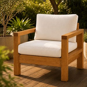 Puede incluir: Un sillón de madera con una estructura robusta de color marrón claro y un diseño cuadrado y macizo. La silla incluye un cojín de asiento grueso de color blanco roto y un cojín de respaldo a juego, ofreciendo un aspecto limpio y neutro.