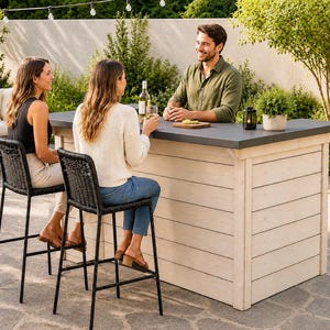 Könnte beinhalten: Ein rechteckiger Outdoor-Bartisch mit einer Basis aus hellen, horizontalen Holzplanken und einer flachen, dunkelgrauen Tischplatte. Die Bar wird durch zwei hohe, schwarze, geflochtene Barhocker mit dünnen Metallbeinen auf einer Steinterrasse ergänzt.