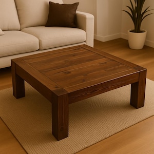 May include: A square, dark brown wooden coffee table with a planked top and sturdy legs. The table is approximately 36 inches square and sits on a neutral-colored rug. The table is in a living room setting.