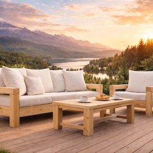 May include: A wooden garden furniture set comprising a sofa, armchair, and coffee table. The set has light-coloured cushions and is on a wooden deck. The background features mountains, a lake, and a sunset.