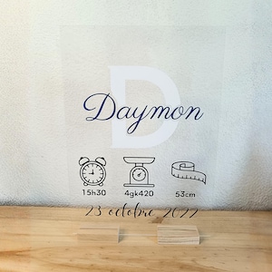 Peut inclure: Panneau acrylique transparent avec le nom "Daymon" en écriture bleu marine, un grand "D" blanc en arrière-plan et des icônes avec des mesures. Le panneau indique l'heure 15h30, le poids 4kg420 et la taille 53cm, avec la date du 23 octobre 2022.