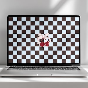 May include: A laptop displays a checkered pattern background with a pair of cherries tied with a bow. The cherries are a deep red color, and the bow is a light pink. The background is a grid of alternating brown and light blue squares.