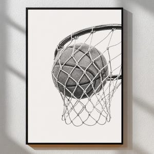 May include: Monochrome framed print featuring a basketball in a net. The ball has a textured surface, and the net is made of woven cords. The background is plain white.