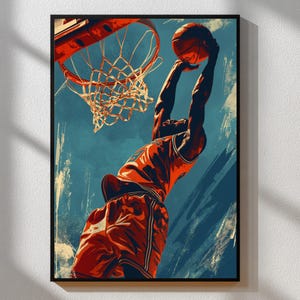 May include: A framed art print showing a basketball player in action, about to dunk the ball. The player is wearing a red uniform. The background is a mix of blue and beige tones, with the basketball hoop and net visible.