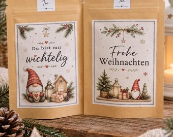 May include: Two light brown paper pouches containing tea. The left pouch is labeled "Früchte Tee" and features a gnome, a house, and the text "Du bist mir wichtig". The right pouch is labeled "Kräuter Tee" and features a gnome, a tree, and "Frohe Weihnachten".