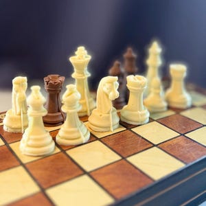 Könnte beinhalten: Ein Schachspiel mit geformten Figuren in Weiß und Dunkelbraun, die auf einem Holzbrett mit Schachbrettmuster angeordnet sind. Die Figuren umfassen Springer, Türme, Läufer und einen König, alle mit sichtbaren Formnähten aus der Herstellung.