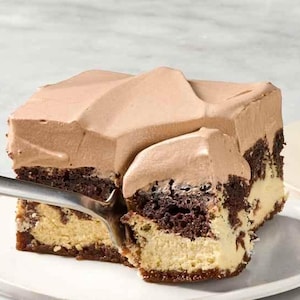 Könnte beinhalten: Ein Stück mehrschichtiger Kuchen mit hellbraunem Zuckerguss und dunkelbrauner Basis. Eine Gabel hebt ein Stück des Kuchens von einem weißen Teller. Ein weiteres Stück Kuchen befindet sich auf einem separaten Teller.