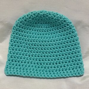 May include: A teal blue crocheted beanie hat. The hat is made with a simple stitch pattern.