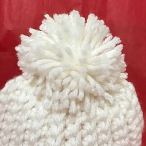 May include: White knitted beanie with a fluffy pom pom on top.