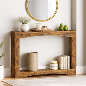 May include: A rustic brown wooden console table with an arched design. The table is decorated with a gold-framed mirror, a white vase with flowers, a woven tray with candles, and decorative items. The table is 122 cm long.