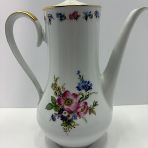 May include: White porcelain coffee pot with a floral design featuring pink, blue, and yellow flowers. The handle and rim are accented with gold trim. The lid has a loop handle.