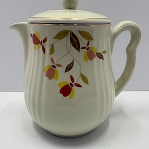 May include: Cream-colored ceramic coffee pot with a lid and handle. The pot is decorated with a floral design in red, yellow, and brown. The rim and handle are trimmed with gold.