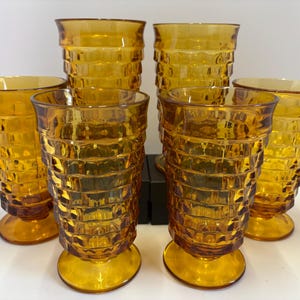 May include: Set of six amber-colored drinking glasses. Each glass has a textured, geometric pattern and a pedestal base. The glasses are approximately 6 inches tall, perfect for serving beverages.