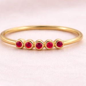 Peut inclure: Une fine bague en or ornée de cinq petites pierres précieuses rouges. La bague a un anneau fin et une finition polie. Les pierres précieuses sont espacées uniformément, créant un design simple mais élégant.