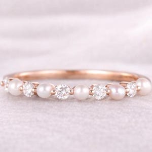 Op de afbeelding: Een roségouden ring met afwisselend parels en heldere edelstenen. De band van de ring is roségoud en de edelstenen en parels zijn gelijkmatig verdeeld. De ring is geplaatst tegen een zachte, witte achtergrond.