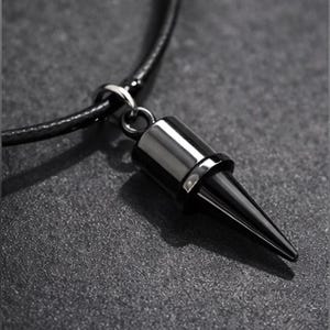 May include: A black and silver pendant necklace. The pendant is a cone shape with a silver top and a black, pointed bottom. The necklace has a black cord and a silver clasp. The background is a textured, dark gray surface.