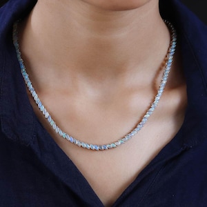 May include: A delicate necklace featuring a series of oval-shaped opals. The opals are set closely together, creating a continuous line of iridescent blue and white gemstones. The necklace is worn around the neck, showcasing its elegant design.