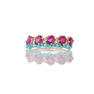 May include: A rose gold ring featuring oval-cut ruby gemstones, small turquoise beads, and tiny diamonds. The ring's design includes a row of rubies, a row of turquoise beads, and a row of diamonds. The ring is displayed on a white background.