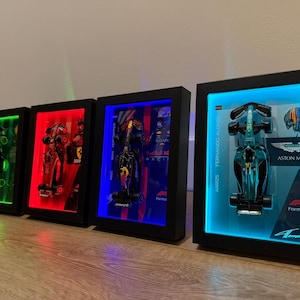 Puede incluir: Cuatro modelos de coches de F&oacute;rmula 1 enmarcados con retroiluminaci&oacute;n LED. Los marcos son negros y los coches se exhiben frente a luces de colores. Un marco presenta un coche Aston Martin con el texto "Fernando Alonso".