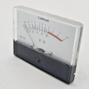 May include: A vintage Calrad VU meter with a clear plastic cover and a black base. The meter face is white with black and red markings, including a needle pointing towards the 2. The text "Calrad" and "VU" are visible.