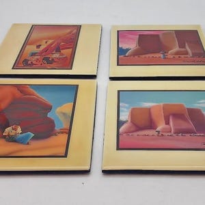 May include: Set of four square ceramic coasters with Southwestern landscape art. Each coaster features a different desert scene with red rock formations, a blue sky, and a beige border. The coasters are ideal for protecting surfaces from drink rings.