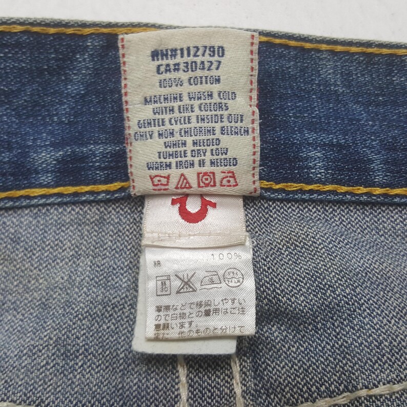 May include: Close-up of a denim jeans tag with care instructions. The tag includes text: "#N112790, CA#30427, 100% COTTON, MACHINE WASH COLD WITH LIKE COLORS, GENTLE CYCLE INSIDE OUT, ONLY NON-CHLORINE BLEACH WHEN NEEDED, TUMBLE DRY LOW, WARM IRON IF NEEDED."