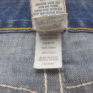 May include: Close-up of a denim jeans label with text. The label includes washing instructions, fabric composition, and the text "MADE IN U.S.A.". The label is white with black text and is attached to blue denim.