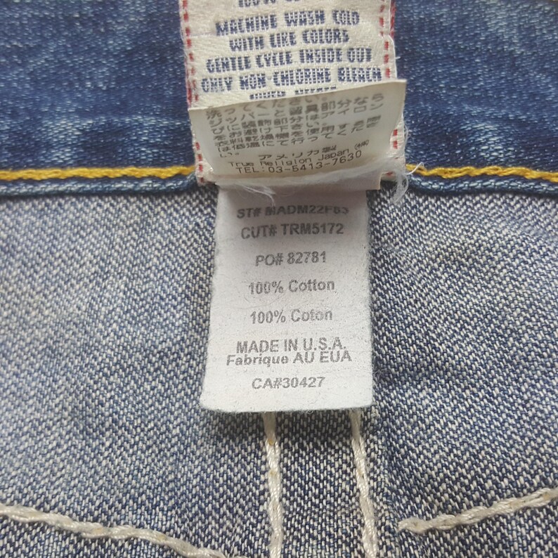 May include: Close-up of a denim jeans label with text. The label includes washing instructions, fabric composition, and the text "MADE IN U.S.A.". The label is white with black text and is attached to blue denim.