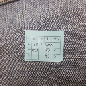 May include: A close-up of a blue and gray textured fabric. A small, rectangular, light green tag is affixed to the fabric. The tag contains black text and numbers, including "C 30", "A 16", "29", "N 25", "L 40.5", and "W 610".