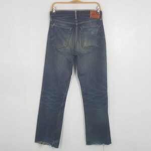 May include: A pair of blue denim jeans featuring a faded wash, two back pockets with reinforced stitching, a brown leather patch on the waistband, and a small red tab on the right pocket. The hem of the pant legs shows a frayed, raw edge finish.