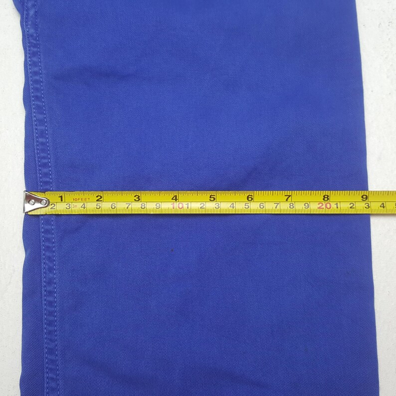 Puede incluir: Primer plano de una tela azul con una cinta m&eacute;trica amarilla y negra. La cinta muestra medidas en cent&iacute;metros, con la tela extendi&eacute;ndose hasta aproximadamente 23 cm.