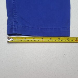 Puede incluir: Primer plano de una secci&oacute;n de tela azul, posiblemente pantalones o pantalones cortos, con una cinta m&eacute;trica amarilla. La cinta muestra medidas en cent&iacute;metros, con la secci&oacute;n de tela midiendo aproximadamente 20 cm de largo.