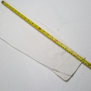 May include: A white long-sleeved shirt with a yellow measuring tape laid across it. The tape shows measurements in inches and feet. The shirt's cuff is visible at the bottom right.
