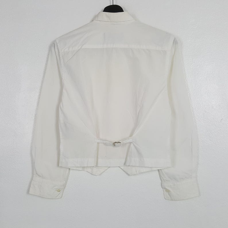 May include: A white ceramic mug with a black handle and the text "But First, Coffee" in a handwritten style. The mug is on a white surface. The mug is approximately 4 inches tall.