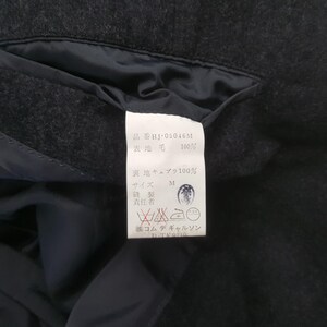 May include: Close-up of a dark gray wool garment tag with Japanese text. The tag includes the product code HJ-05046M, fabric composition, size M, and care symbols. The garment appears to be a jacket or coat.